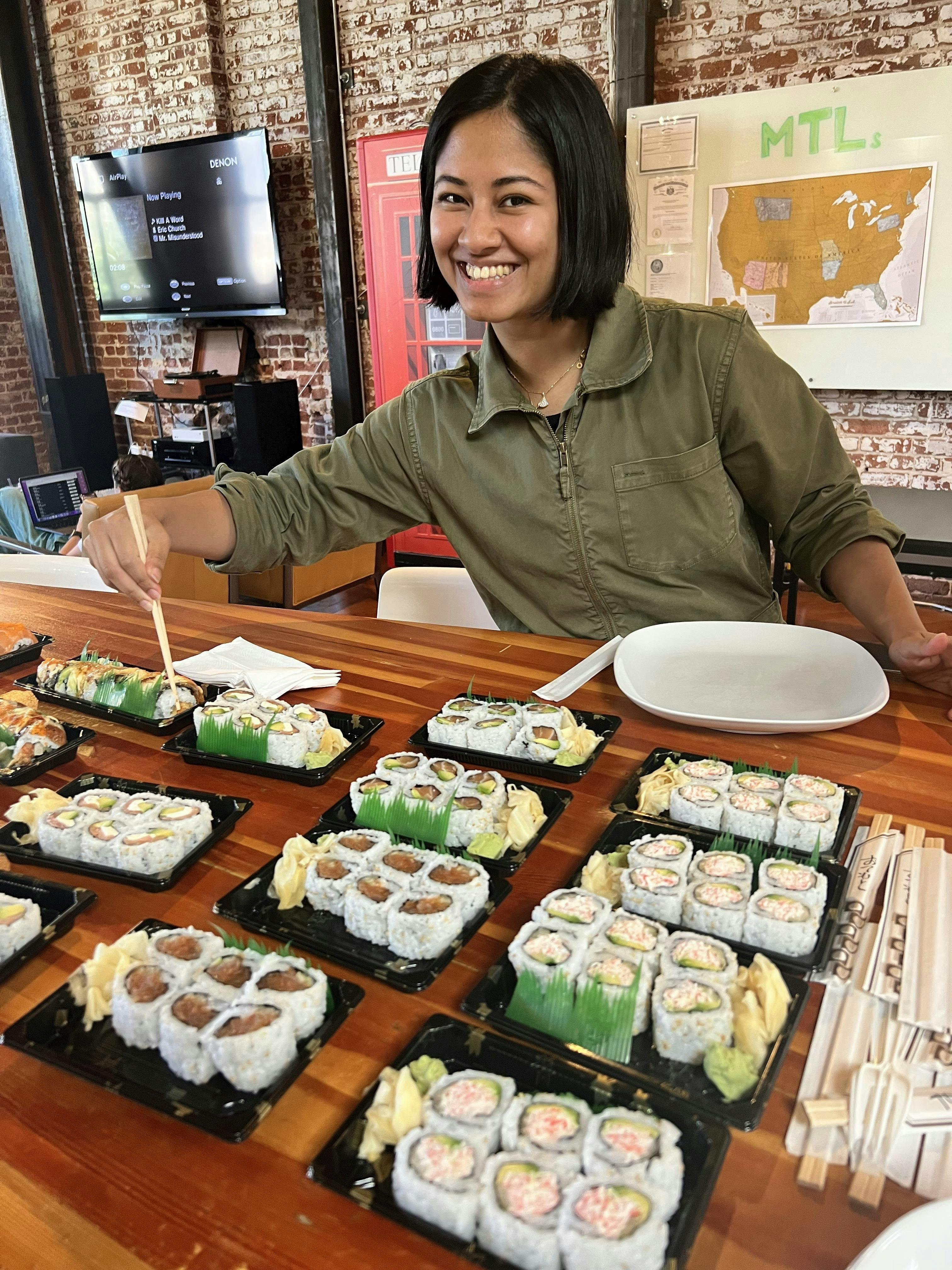 Woman smiling at the camera, holding chopsticks over a table full of sushi